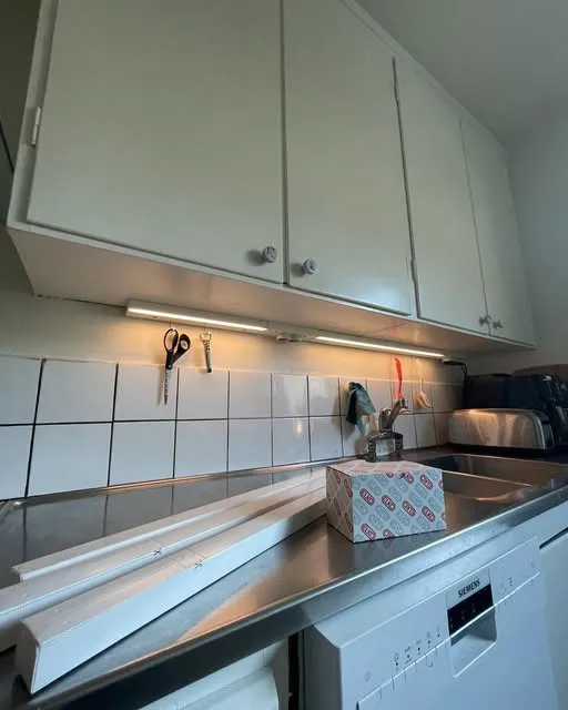 Kök med vita överskåp och lysrörsarmaturer monterade under skåpen