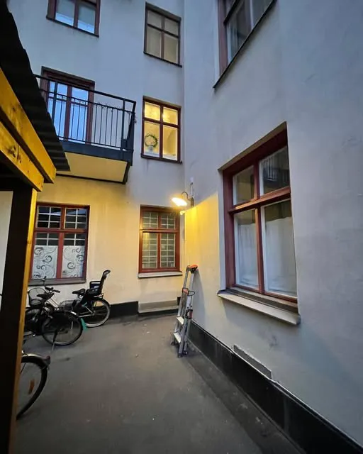 Innergård i kvällsljus med en tänd vägglampa på fasaden och en stege lutad mot väggen